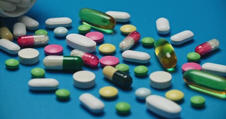 Close-up image of multi-colored tablets spilling out of open bottle onto blue surface