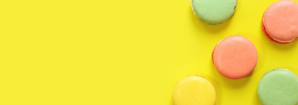 Bright French macarons on yellow background, top view. Assortment of multi-colored macarons with different flavors. Delicious pastries, flat lay. Food background. Sweets
