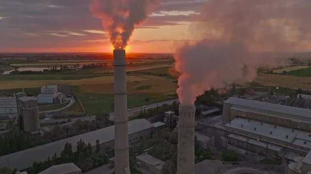 setting sun behind of smoke and steam out of soviet concrete factory pipe, aerial view
