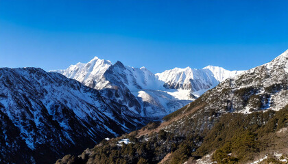 A majestic snow-covered mountain range with sharp, towering peaks under a clear blue sky