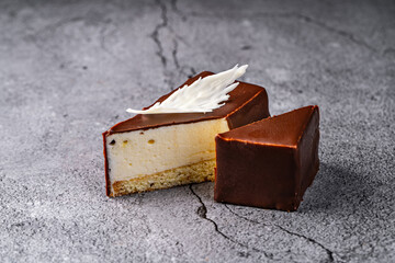 Chocolate-covered cheesecake slice with white chocolate decoration on a textured gray background
