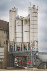 Industrial silos in a recycling facility with aged surfaces, located in an industrial zone with cloudy weather.