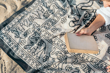 Woman holding antique book on elephant patterned beach towel