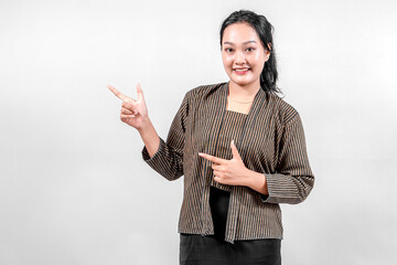 An Indonesian woman wearing traditional lurik attire smiles brightly while pointing with both...