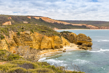 Rugged cliffs rise above tranquil waves, revealing a secluded beach in Port Campbell National Park at the Great Ocean Road.