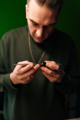 Vertical portrait of concentrated technician carefully examining motherboard, troubleshooting issues in professional electronics repair workshop with green wall, selective focus, blurred background.