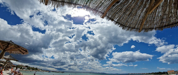 Sunny beach day with dramatic clouds and straw parasols