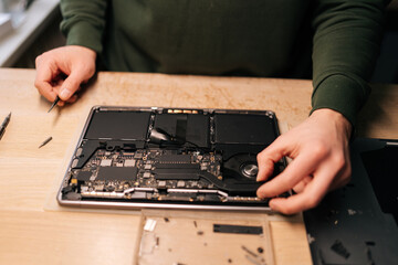 Top view of unrecognizable technician meticulously working on laptop motherboard, using tweezers...