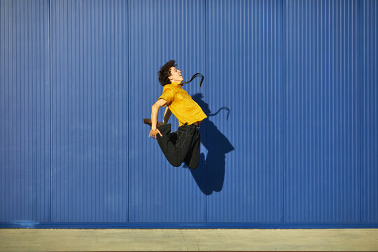 Student performing an energetic jump against a vibrant blue backdrop showcasing youthful enthusiasm and athleticism in a lively setting