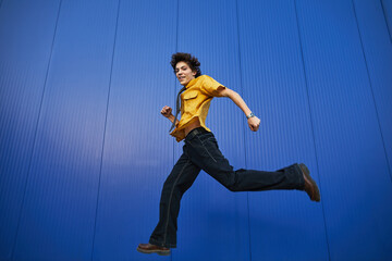 Young student runs energetically against a vibrant blue wall on a sunny day