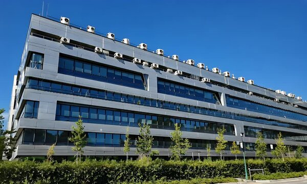 A modern multi-story office building with a sleek facade and many air conditioning units.