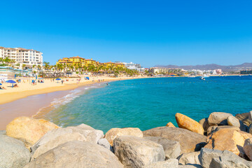 Fototapeta premium The sandy Playa El Farito beach along the touristic coastline full of resorts, seaside cafes and markets in Cabo San Lucas, Mexico.