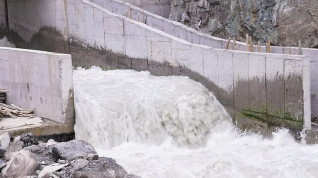 Partially built small hydropower plant on a mountain river. Concrete channel directs water flow through the structure. Shot in slo-mo at 120 fps.