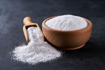 salt in a wooden bowl on a black stone table, selective focus.