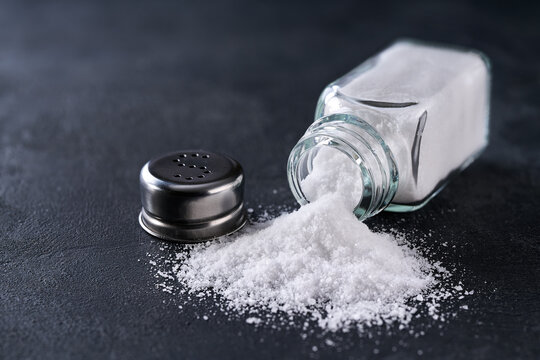 Spilled salt and salt shaker on on a black stone table, selective focus.