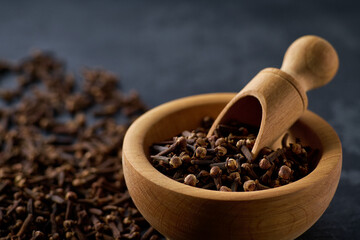 Wooden bowl with cloves spice on a black kitchen table, selective focus.