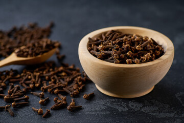 cloves spice in a wooden bowl on a black stone table, selective focus.