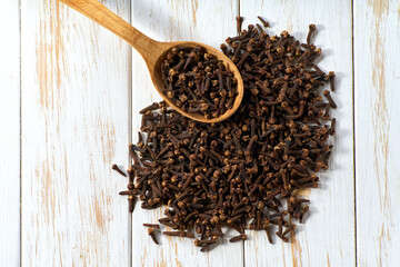cloves spice in a wooden spoon on a light kitchen table, top view.