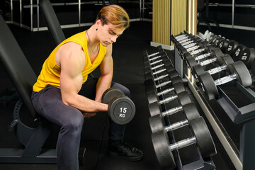 Young guy in a yellow t-shirt lifting weights in a gym next to some dumbbells