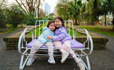 Two young girls are sitting on a bench in a park