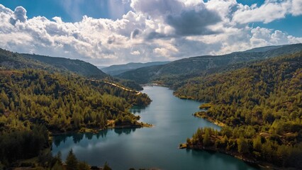 Aerial view of a serene lake surrounded by lush green forests and rolling hills.