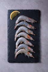 Fresh king prawns on black stone board on grey background. Top view.