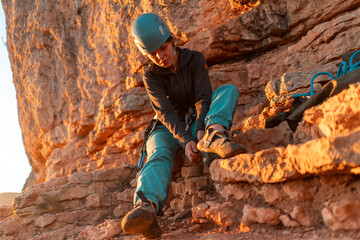 Young girl is preparing for training on the rocks sunset, in the mountains and puts a helmet ....