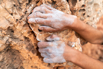Young girl is engaged in extreme sports, fearlessly climbs up the rock using white magnesia powder, holds her hand to the ledge in the relief,