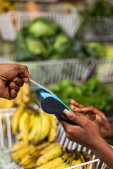 A customer makes contactless card payment via Point Of sale (POS) terminal, at fresh produce market...