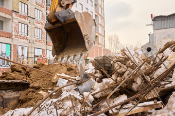 An excavator is digging through construction debris in an urban setting, assisting the task