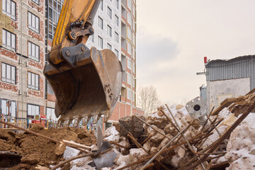 An excavator is digging through construction debris in an urban setting, assisting the task