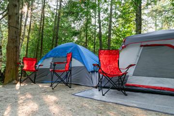 A picturesque summer camp in the heart of the forest, bathed in sunlight., complete with a camping tent and chairs