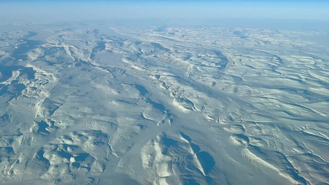high level flying across Canadian tundra landscape in Nunavut and Northwest Territories with fully snow-covered mountains and deeply frozen lakes and rivers - wide angel 4k aerial video footage