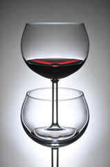 Two wineglasses one standing in the bowl of another - the top glass is full of red wine