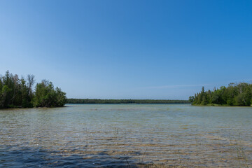 Stunning lake shimmering under the bright summer sun, surrounded by lush greenery and clear blue skies.