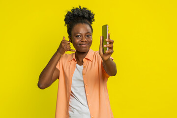 African American woman holds smartphone and makes call me gesture, signaling a desire for...