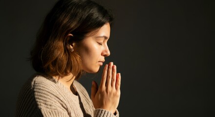 Peaceful reflection of young hispanic female in prayer pose against dark background