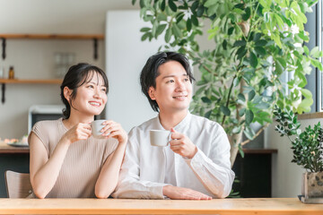 家のリビング・ダイニングでくつろぐ仲良しの若い日本人夫婦
