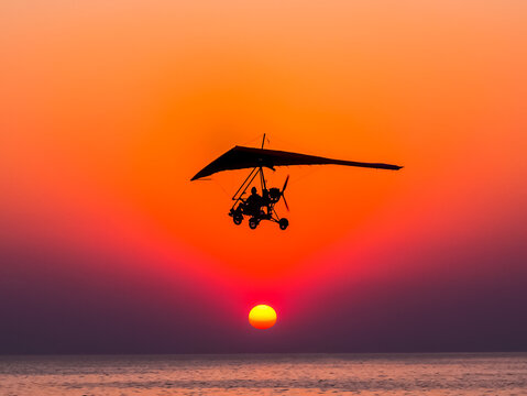Motorized glider flies against the sunset over the sea.