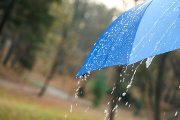 Open blue umbrella under pouring rain outdoors, closeup. Space for text