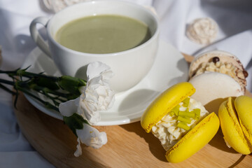 Nutrient-rich matcha drink with trendy macaron dessert on wooden tray in bed with fresh flowers. Morning beautiful breakfast present gift idea. Vibrant creative colors. Natural energy givers tea