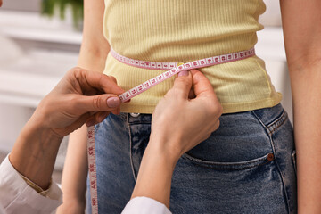 Weight loss. Nutritionist measuring patient's waist with tape in clinic, closeup