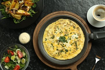 Tasty brunch. Delicious omelette, salad, fried potatoes and coffee served on black textured table, flat lay