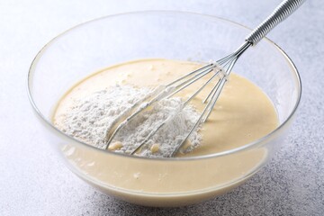 Whisk and bowl of dough on grey table, closeup