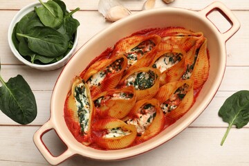 Delicious pasta with ricotta cheese, spinach and tomato sauce in baking dish on wooden table, flat lay