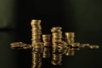 Many stacked coins on dark mirror surface, closeup