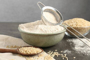 Brown rice, flour and sieve on grey table, closeup