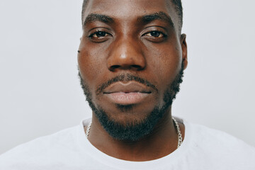 Obraz premium Portrait of a serious young man with a confident expression, wearing a plain white shirt against a soft white background, showcasing strong features and natural beauty