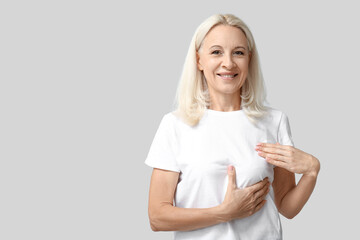 Mature woman checking her breast on grey background. Cancer awareness concept