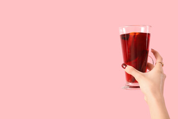 Female hand with glass of warm mulled wine on pink background
